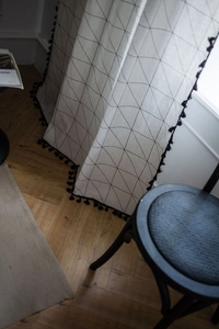 Detail of white cotton linen curtain with geometric patterns and black fringe tassels
