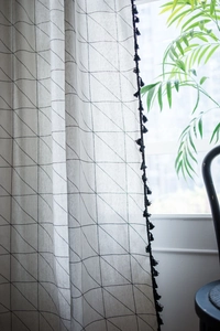Detail of geometric printed linen curtain with black tassel fringe and mesh pattern