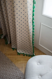 Dettaglio tenda in cotone lino beige con stampa floreale blu e bordo con nappe verdi