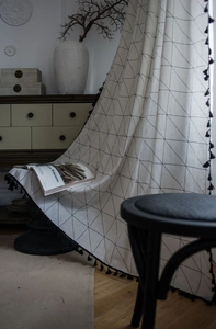 Detail of off-white cotton linen fabric with black geometric grid and tassel trim