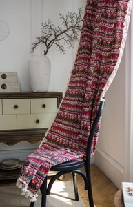 Close-up of Bohemian red floral print curtain with fringe details on a black chair