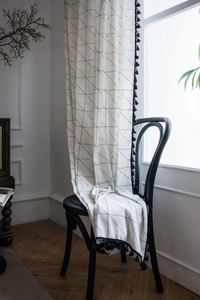 Detail of off-white cotton linen curtain with black geometric patterns and tassel edges