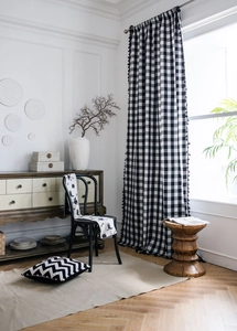 Detail of black and white gingham curtain with fringe tassels and natural linen texture