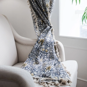 Blue William Morris pattern cotton linen curtain with tassels on a beige sofa