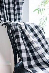 Detail of black and white plaid cotton linen curtain with decorative fringe on a chair