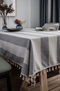 Detailed view of grey striped linen tablecloth featuring cream tassel fringe on wooden table