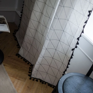 White cotton linen curtain with black geometric patterns and tassel trim on wooden floor