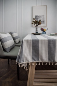 Detail of grey striped Nordic tablecloth with beige fringe tassels and matching pillows