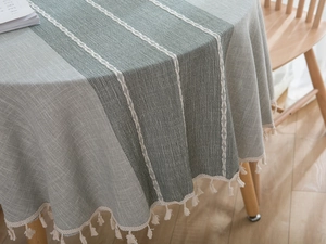 Detailstruktur der graugrünen Tischdecke aus Baumwollleinen mit weißen Quastenfransen
