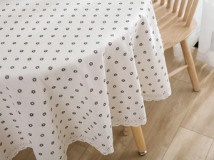 Close-up of beige cotton linen tablecloth with daisy print and white lace floral edges