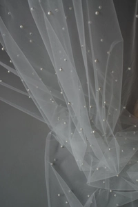 Macro shot of elegant white sheer mesh fabric with glossy pearl beads and fine texture