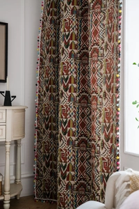 Detail of bohemian curtain featuring colorful geometric patterns and decorative pom-pom trim