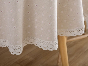 Close-up of beige linen tablecloth featuring white daisy prints and scalloped lace trim
