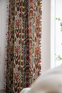 Detail of bohemian geometric curtains featuring colorful pom-pom fringe and woven texture