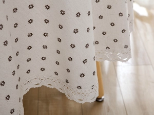 Detailed view of beige cotton linen tablecloth featuring small brown floral patterns and lace