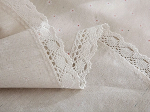 Detail of linen tablecloth with daisy floral print and delicate white lace edges