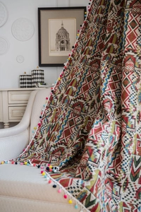 Detail of bohemian geometric knit throw blanket with colorful pompom fringe on a chair