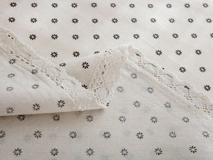 Detailed close-up of beige linen tablecloth with daisy print and white lace crochet edge