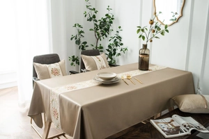 Detailed close-up of beige tablecloth and matching pillows with elegant floral embroidery