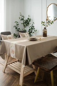 Detailed view of beige tablecloth featuring elegant floral embroidery on a dining table