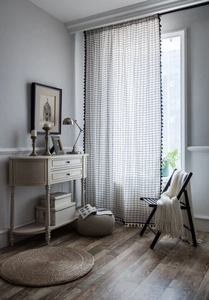 Close-up of white grid pattern fabric with black pom-pom tassel trim for curtains