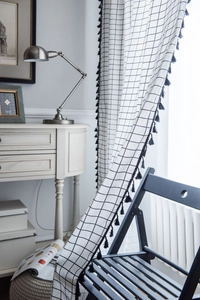 Detail of white checkered curtain featuring decorative black tassels and a soft fabric texture