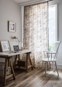 Detailed close-up of floral cotton linen curtain with decorative black pom-pom tassels