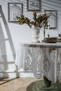 Detailed close-up of white lace round tablecloth with floral vine embroidery patterns
