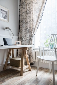 Detail of floral print curtain with black tassel fringe on cream cotton linen fabric