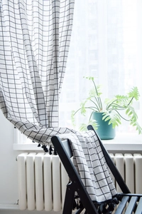 Detail of white plaid curtains featuring black grid patterns and elegant tassel fringe edges