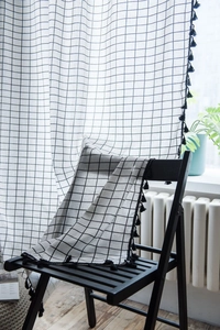 Detail of white plaid curtain with black grid pattern and decorative tassel trim edge