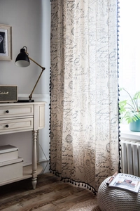Close-up of linen curtain with black vintage letter prints and tassel ball fringe
