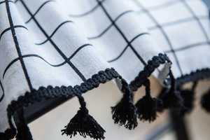 Detail of white grid fabric with black ball tassels and cotton linen texture