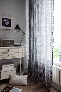 Detail of grey herringbone cotton linen curtain with black tassel fringe on the edge