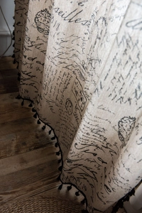 Close-up of linen curtain fabric with vintage French text and black tassel fringe