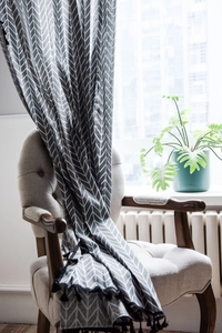 Detail of grey geometric herringbone curtain with black tassel fringe on cotton linen fabric