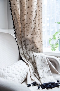 Detail of linen texture curtain with dandelion prints and decorative black fringe tassels