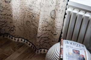 Close-up of beige linen curtain with vintage black script and stylish pompom tassels