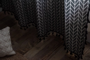 Detail of grey cotton linen curtain with white chevron pattern and black tassels on edge