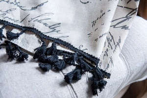 Close-up of cotton linen fabric texture with black script print and tassel fringe details