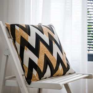 Bohemian square throw pillow with golden wave geometric patterns on a wooden chair