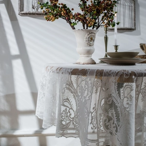 Elegant white lace round tablecloth with hollow flower patterns on wooden table