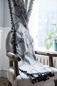 Détail d'un rideau en coton et lin gris damassé avec franges à pompons noirs