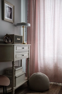 Detail of pink plaid linen curtain with decorative fringe in a warm sunlit interior