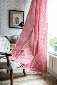 Close-up of red gingham curtain fabric featuring cream tassel fringe in a cozy room
