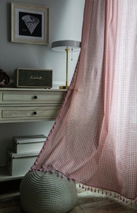 Detail of pink gingham cotton linen curtain with tassel trim showing semi-sheer fabric texture