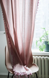 Detail of pink gingham curtain with decorative tassels on a light cotton linen fabric