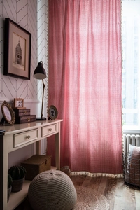 Close-up of red gingham window curtain featuring decorative beige tassel edges and fabric texture