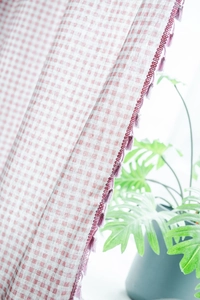 Detail of pink gingham cotton linen curtain with purple fringe trim and natural leaf