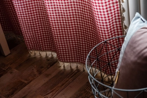 Detailed view of red checkered cotton curtain featuring decorative beige fringe tassels